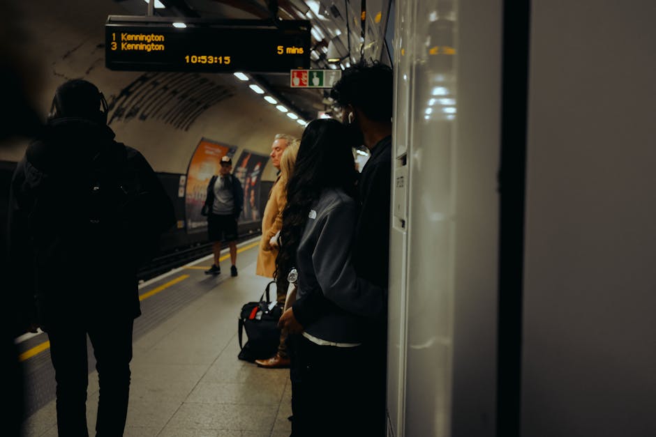 Interior view of a London Underground station platform at High Street Kensington, with a yellow and white train stationary on the left side. The platform has a tactile paving strip along the edge for
